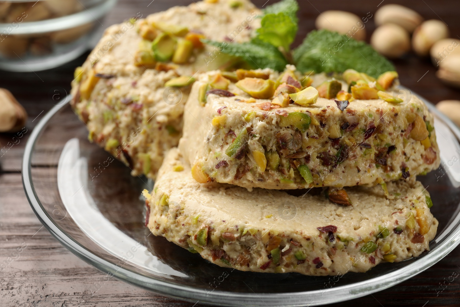 Photo of Tasty halva with pistachios and mint on wooden table, closeup