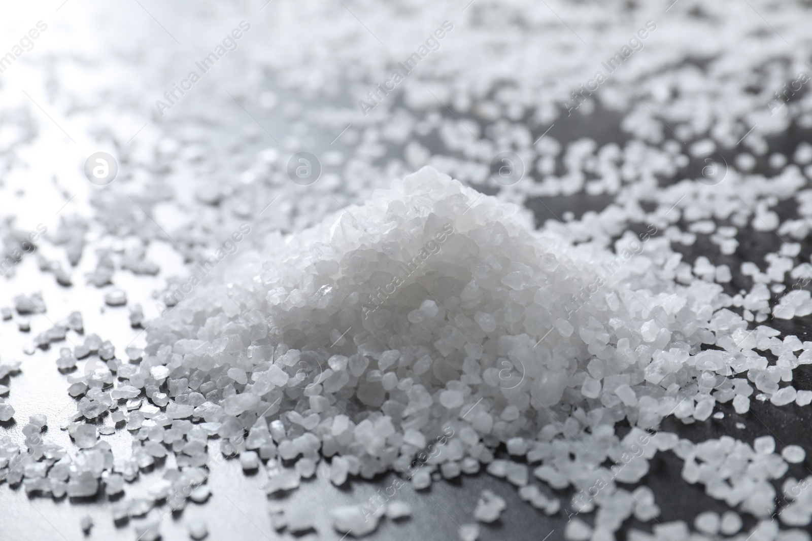 Photo of Heap of natural salt on black table, closeup