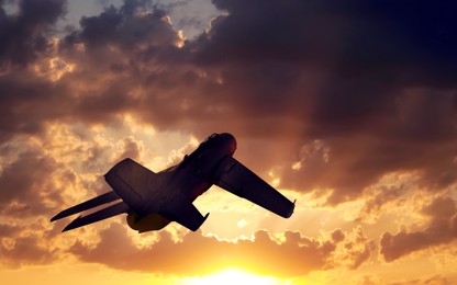Silhouette of jet fighter in cloudy sky at sunset