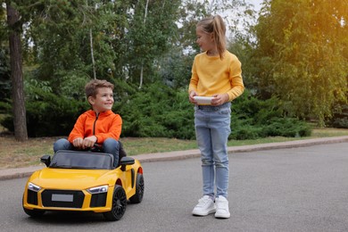 Cute girl operating children's car with little boy outdoors