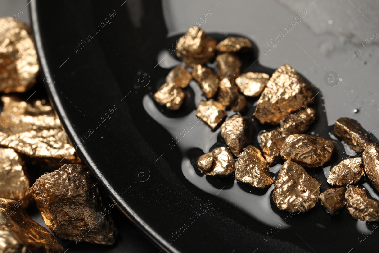 Photo of Plate with gold nuggets on black table, closeup