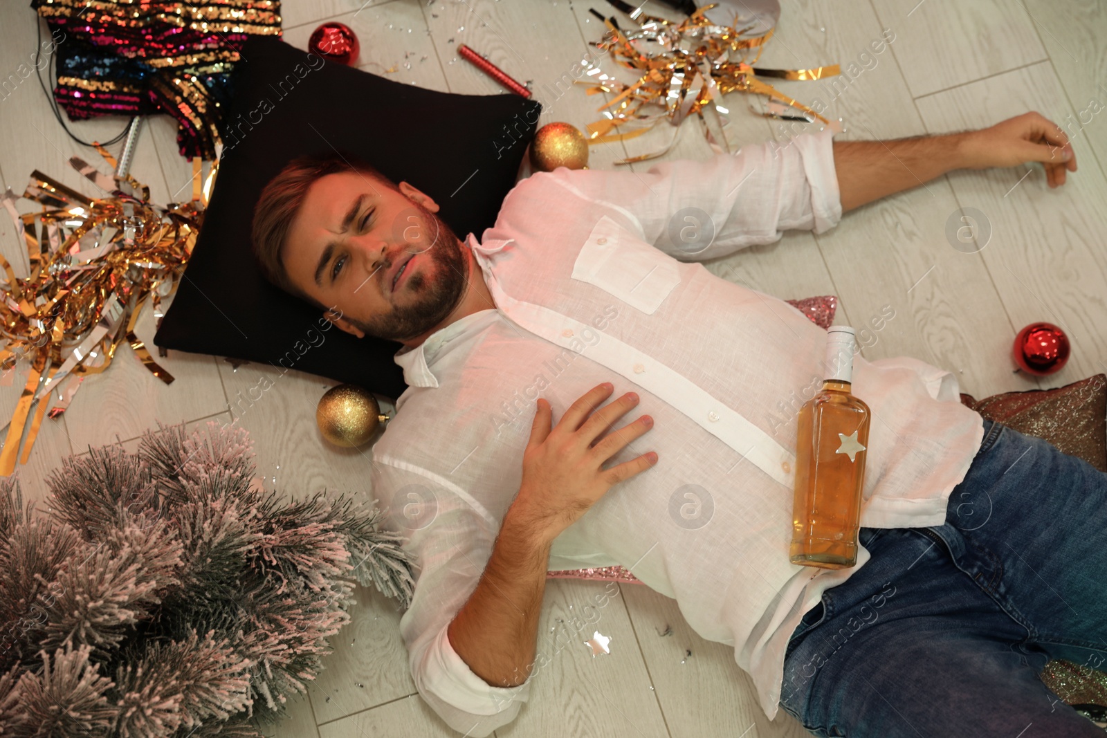 Photo of Young man suffering from hangover in messy room after New Year party, above view