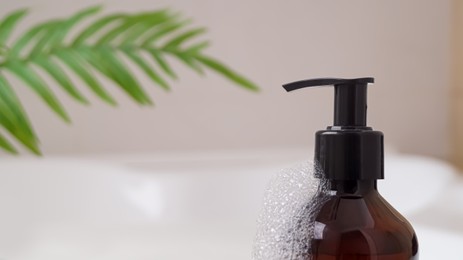 Photo of Bottle of bubble bath with foam on tub indoors, closeup. Space for text