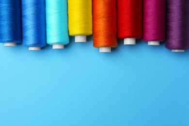 Set of different colorful sewing threads on light blue background, flat lay. Space for text