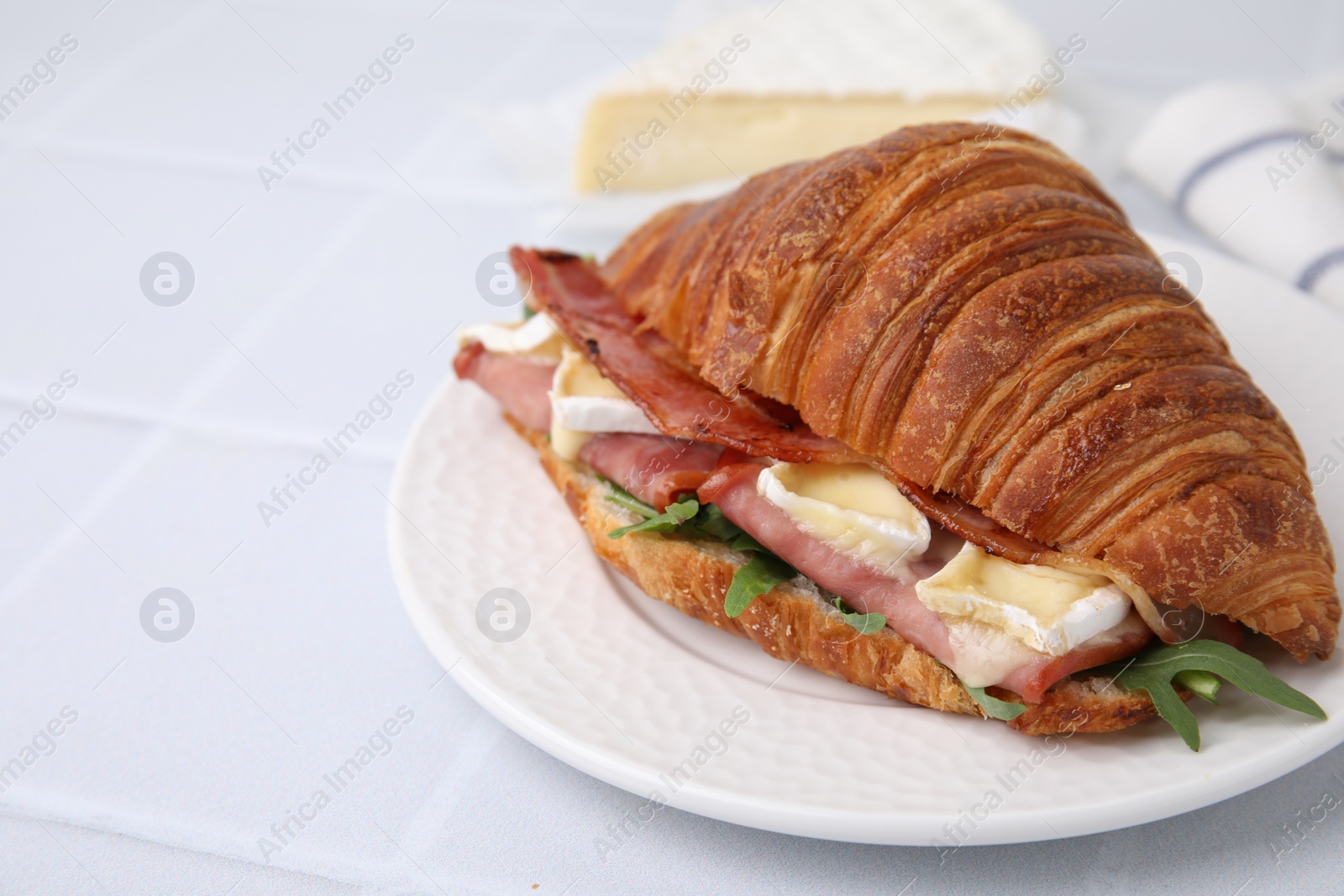 Photo of Tasty croissant with brie cheese, ham and bacon on white tiled table, closeup. Space for text