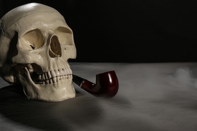 Photo of Human skull with pipe and smoke on black background. Space for text