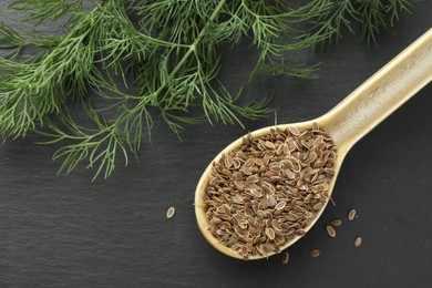 Photo of Spoon with dry seeds and fresh dill on black table, flat lay