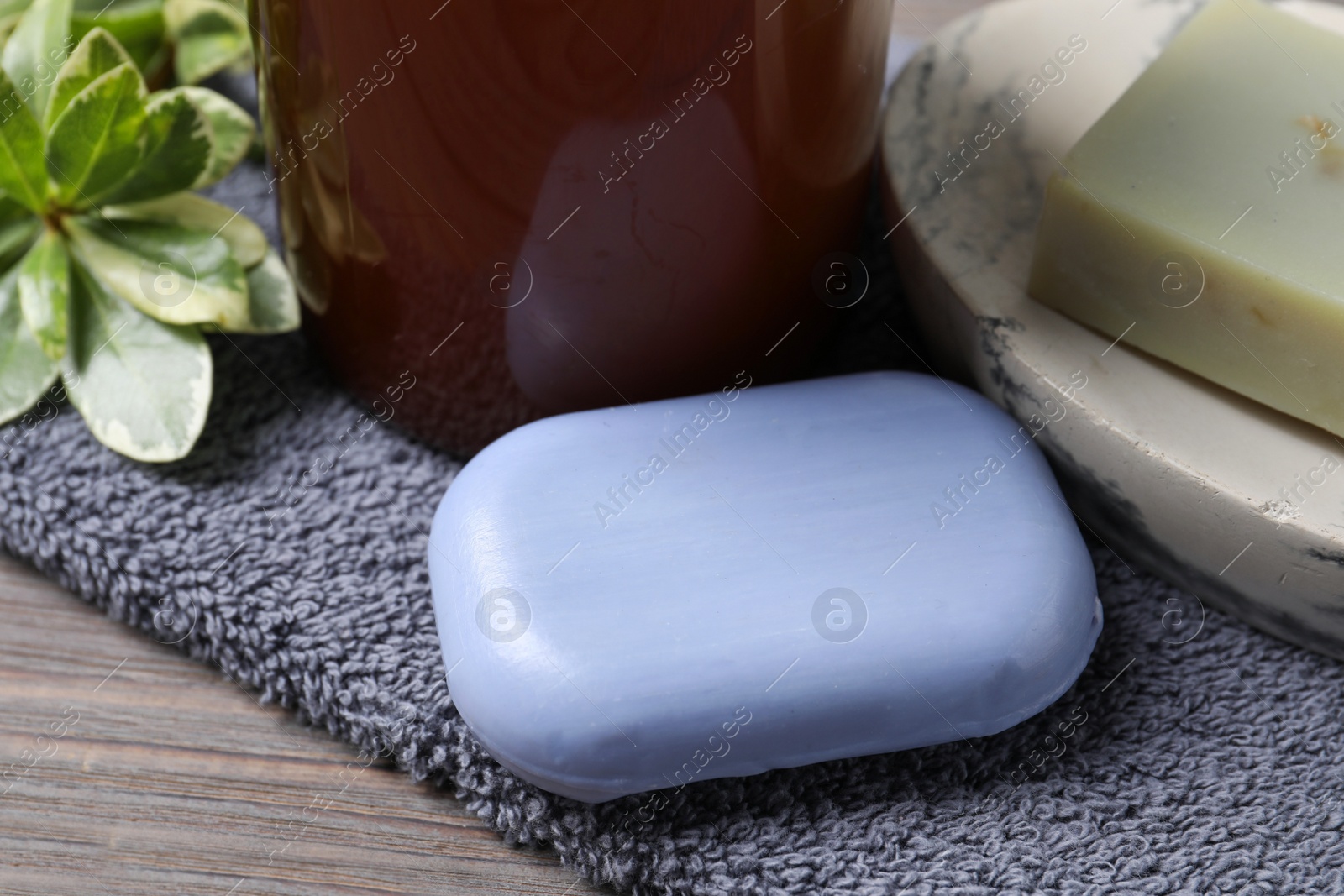 Photo of Soap bars, green plant and terry towel on wooden table, closeup