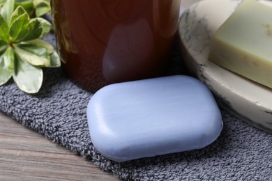 Photo of Soap bars, green plant and terry towel on wooden table, closeup