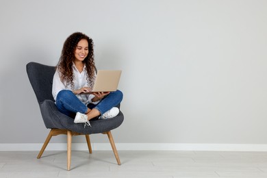 Photo of Young African-American woman working on laptop in armchair indoors. Space for text