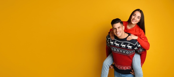 Photo of Couple in Christmas sweaters on yellow background, space for text