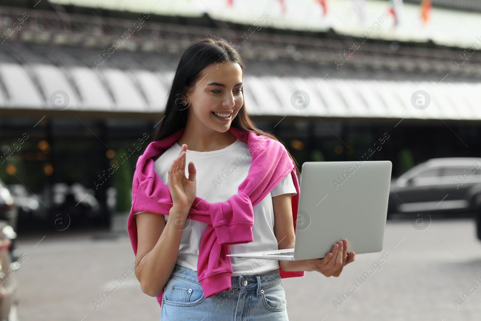 Photo of Happy young woman using laptop for video chat on city street