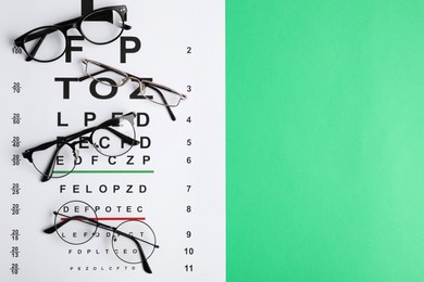 Photo of Vision test chart and glasses on green background, flat lay. Space for text