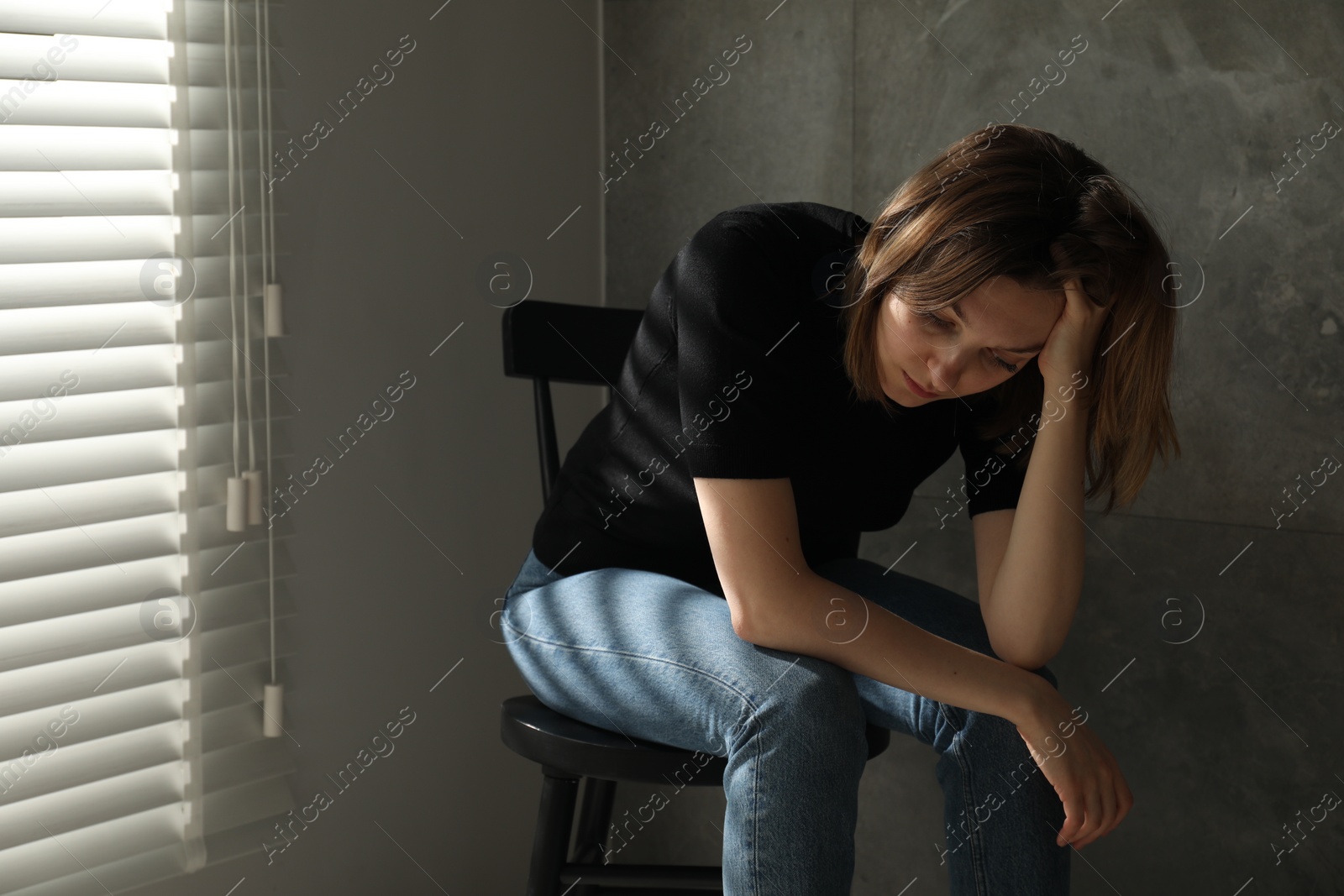 Photo of Sad young woman sitting on chair indoors, space for text