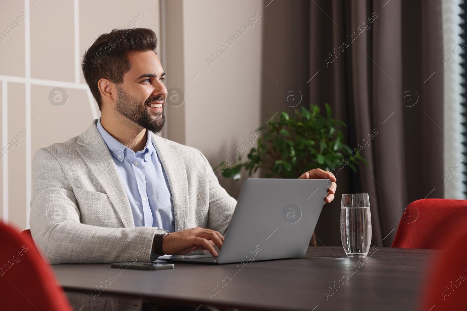 Photo of Happy young man with laptop at table in office