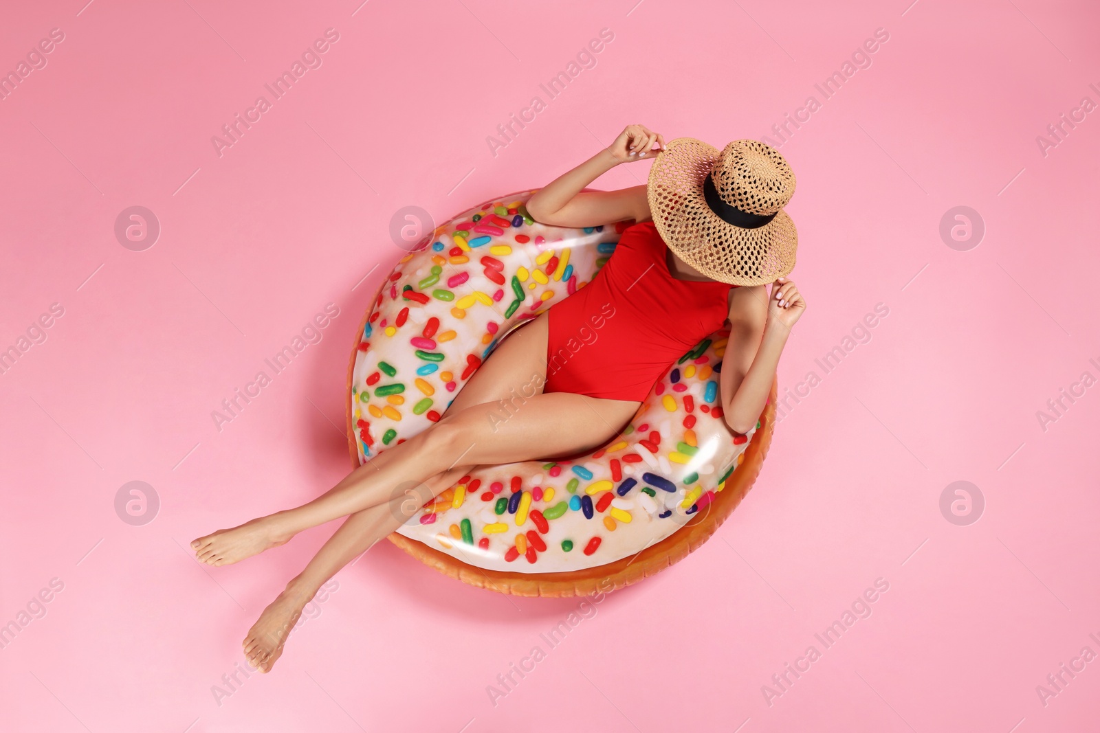 Photo of Young woman in stylish swimsuit on inflatable ring against pink background, top view