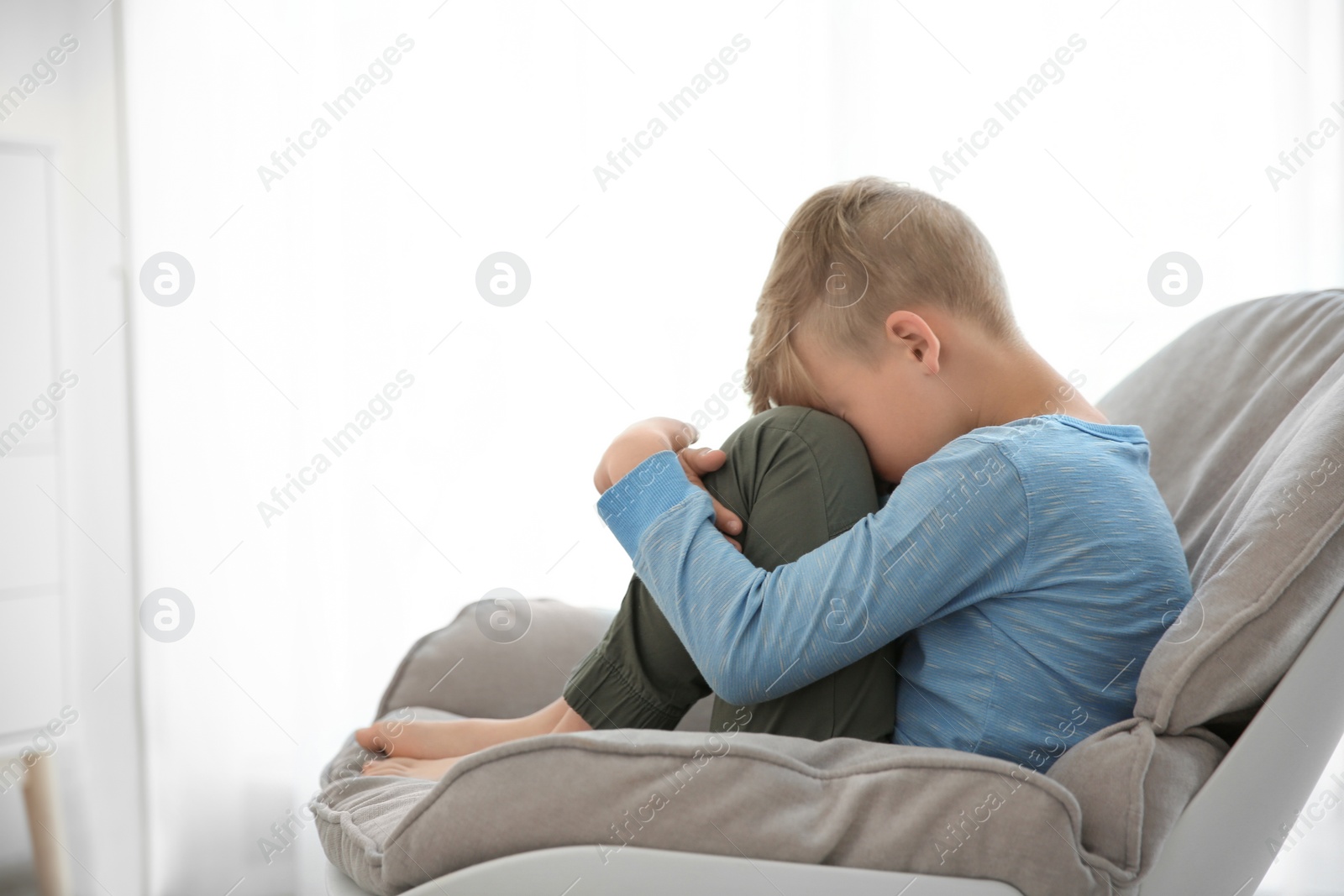 Photo of Lonely little boy sitting on chair at home. Autism concept