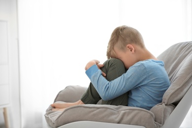 Photo of Lonely little boy sitting on chair at home. Autism concept