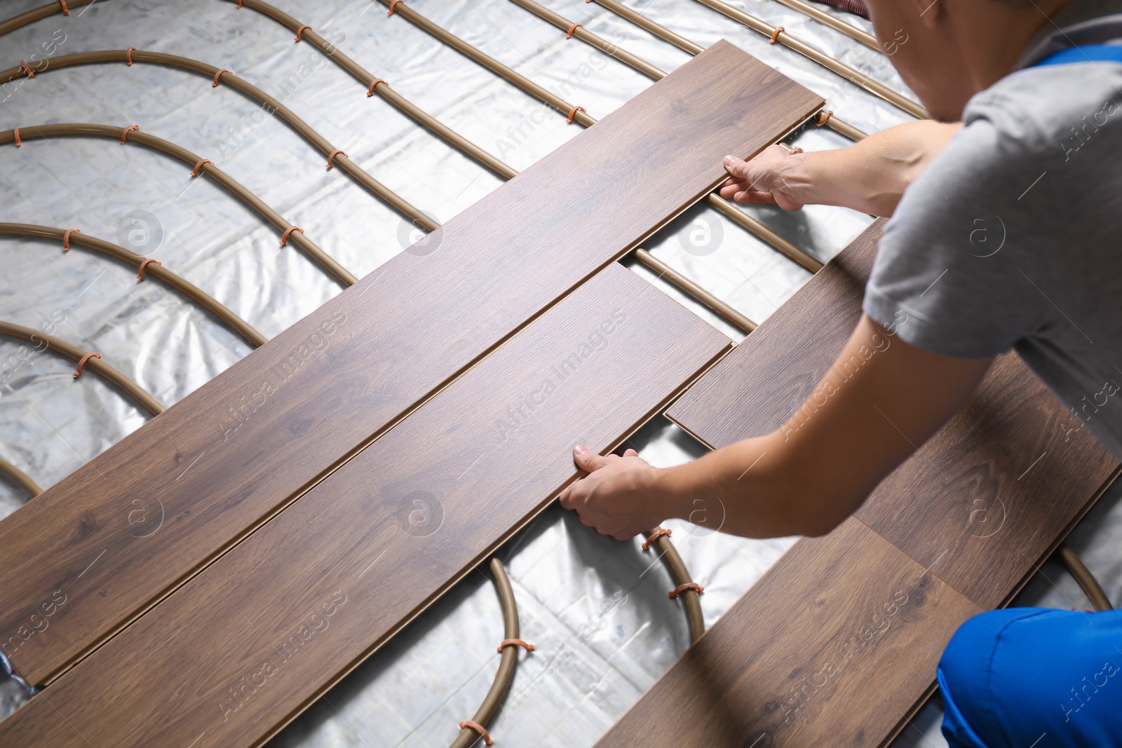 Photo of Worker installing new wooden laminate over underfloor heating system, closeup