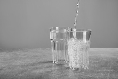 Photo of Pouring soda water into glass on grey table. Space for text
