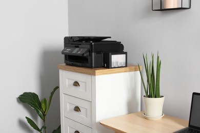 Photo of Modern printer on chest of drawers near wooden table indoors