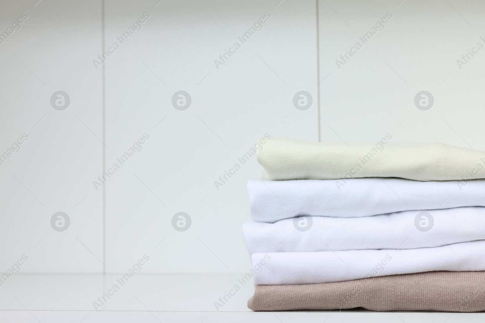 Photo of Stack of different folded shirts on white shelf, space for text. Organizing clothes