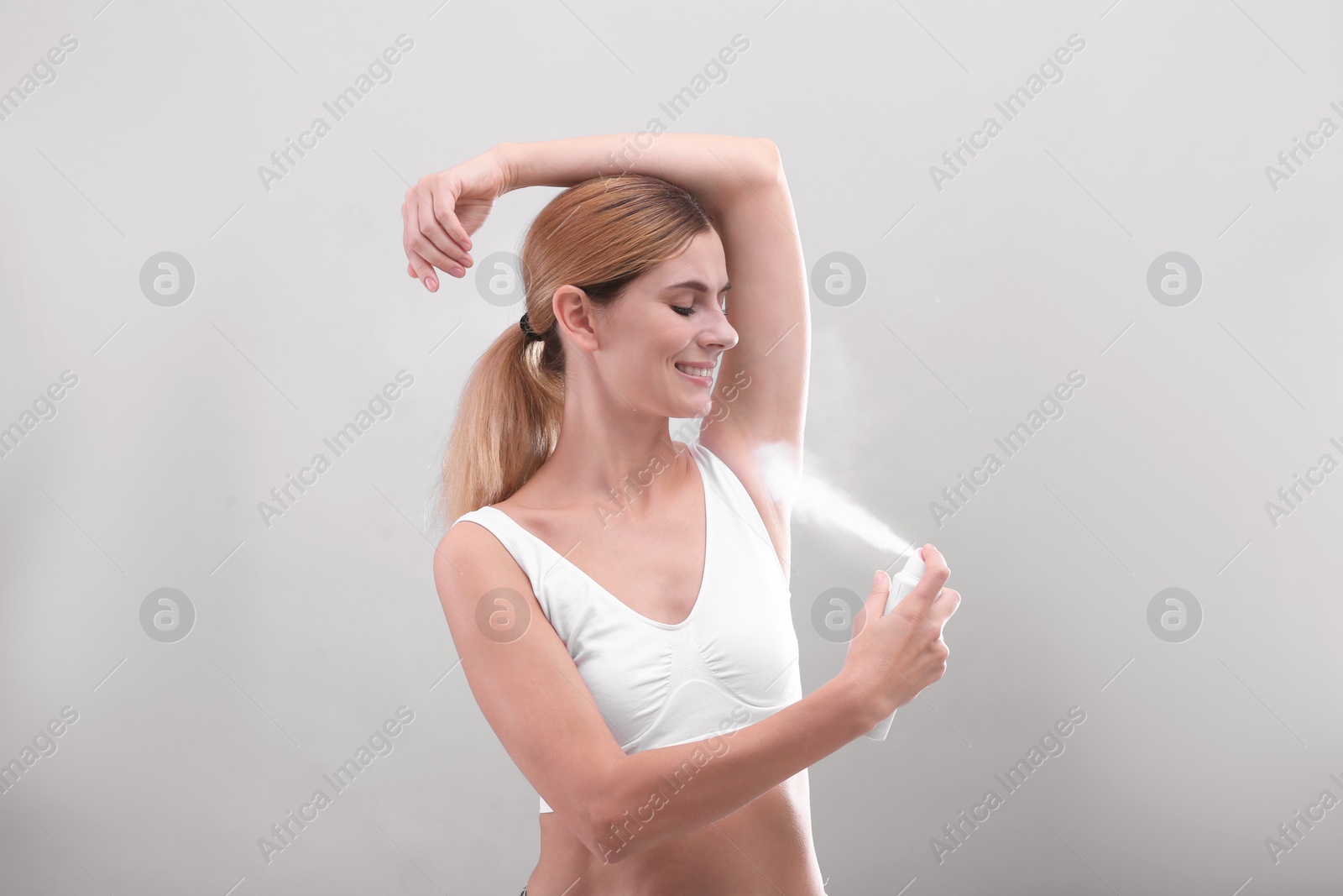 Photo of Young woman using deodorant on grey background