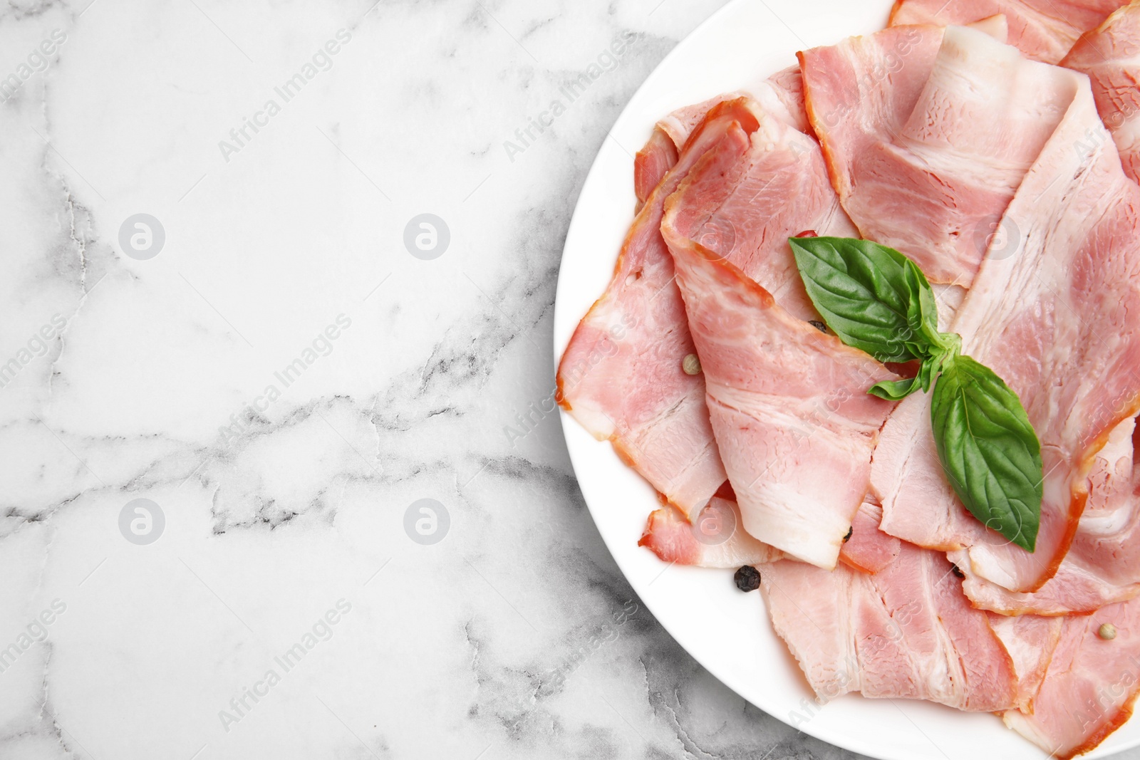 Photo of Plate of sliced raw bacon on white marble table, top view. Space for text