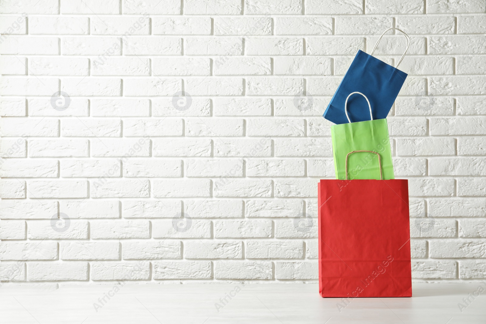 Photo of Colorful paper shopping bags on table against brick wall. Space for text