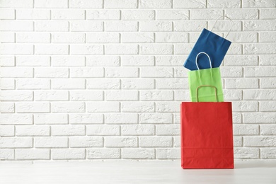 Colorful paper shopping bags on table against brick wall. Space for text