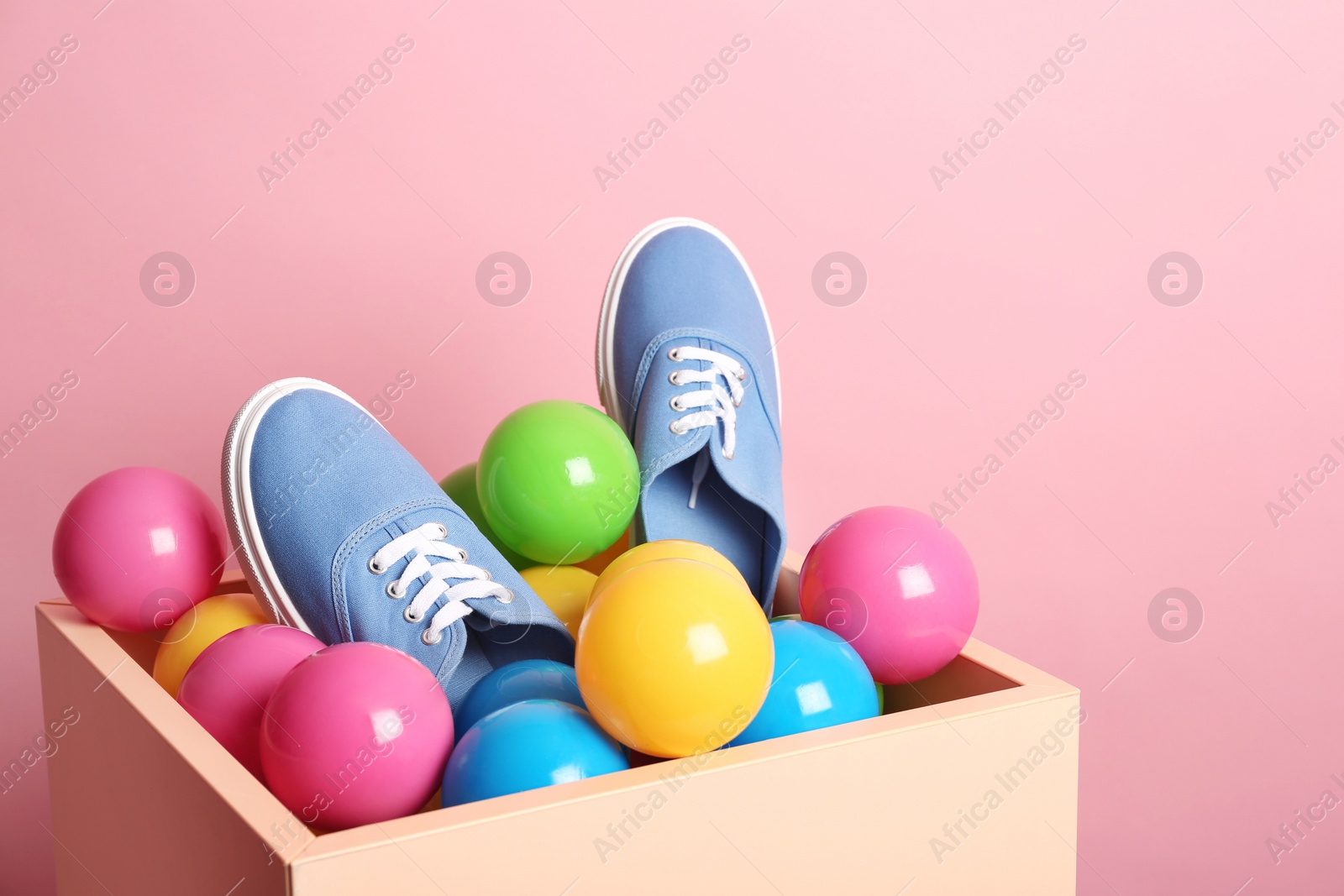 Photo of New sneakers in box with plastic balls on color background, space for text