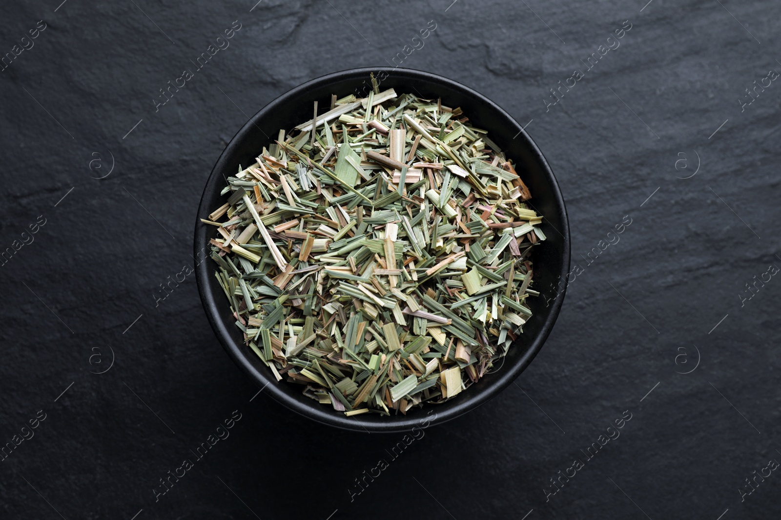 Photo of Bowl with aromatic dried lemongrass on black table, top view