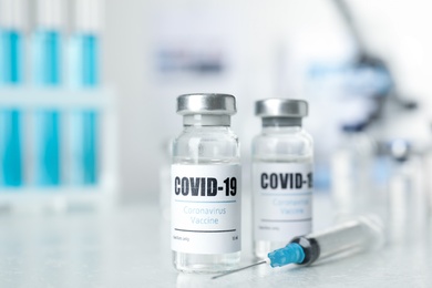 Photo of Vials with vaccine against Covid-19 and syringe on white table indoors