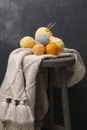 Photo of Woolen yarns with knitting needles and scarf on stand near black wall