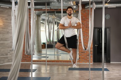 Young man practicing fly yoga on hammock in studio