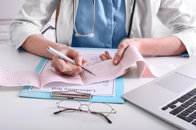 Doctor examining cardiogram at table in clinic, closeup