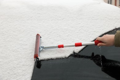 Woman cleaning car windshield from snow with squeegee, closeup