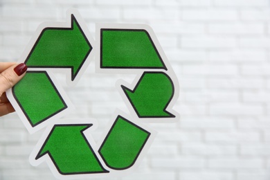 Woman holding paper recycling symbol on light background, closeup. Space for text