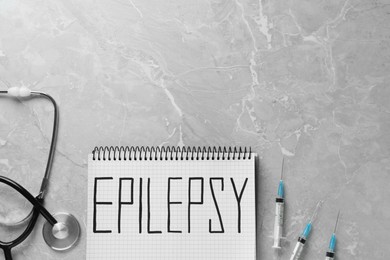 Notebook with word Epilepsy, stethoscope and syringes on grey marble table, flat lay. Space for text