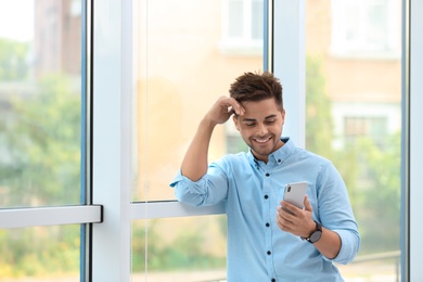 Photo of Portrait of handsome young man with smartphone near window