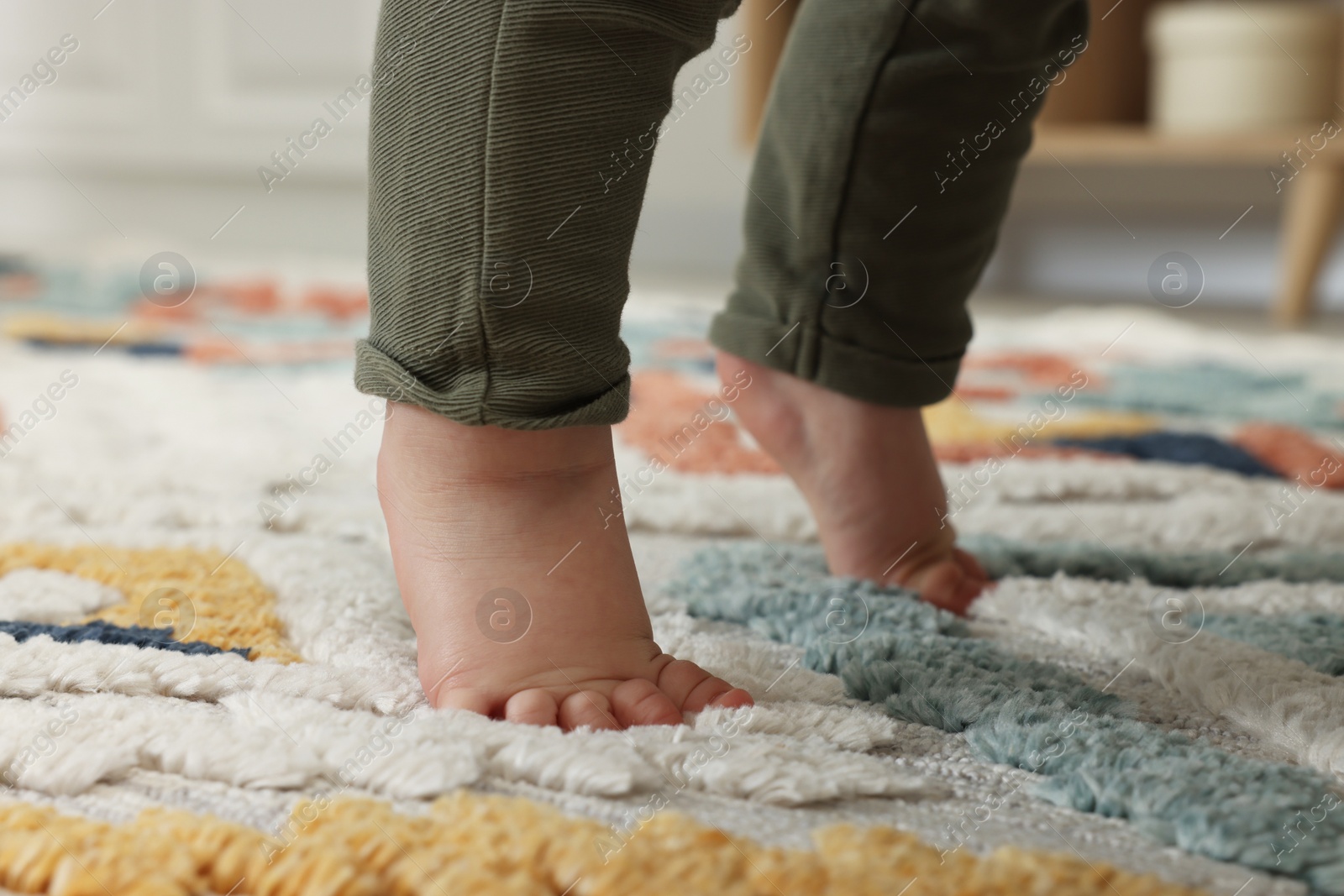 Photo of Baby standing on soft colorful carpet, closeup