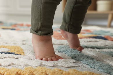 Photo of Baby standing on soft colorful carpet, closeup