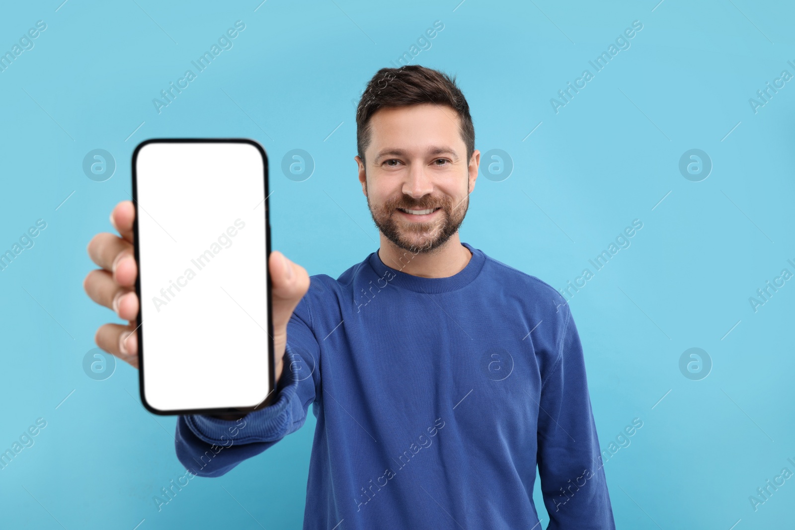 Photo of Handsome man showing smartphone in hand on light blue background