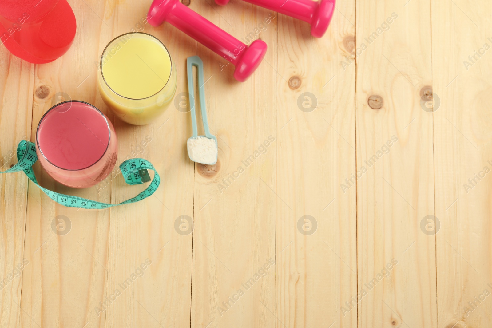 Photo of Tasty shakes, dumbbells, measuring tape and powder on wooden table, flat lay with space for text. Weight loss