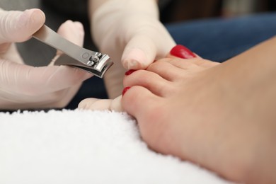 Photo of Pedicurist cutting client`s toenails with clipper in beauty salon, closeup