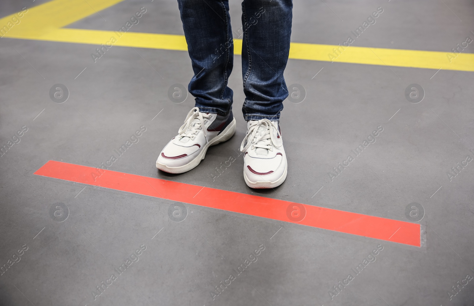 Photo of Person standing behind taped floor marking indoors for social distance, closeup. Preventive measure during coronavirus pandemic