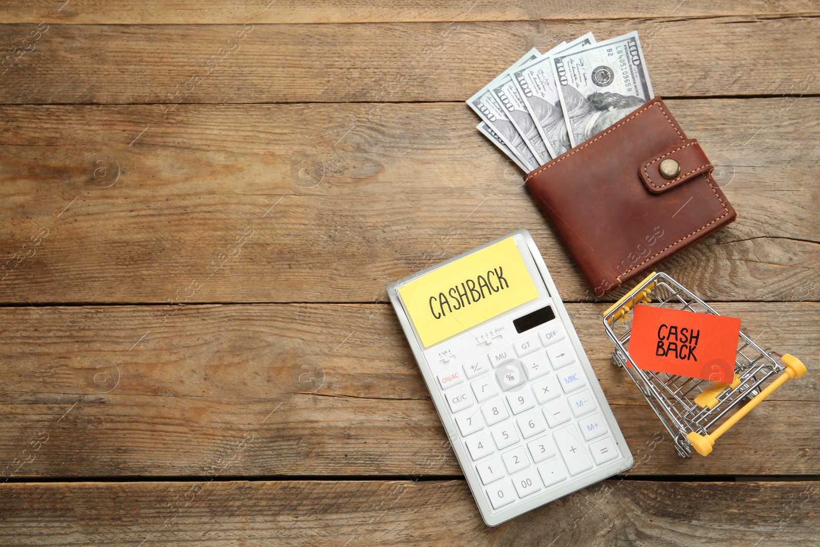 Photo of Dollar banknotes in wallet, calculator and shopping cart on wooden background, flat lay with space for text. Cashback concept