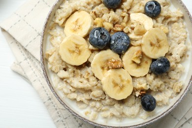 Photo of Tasty oatmeal with banana, blueberries, walnuts and honey served in bowl on white wooden table, top view