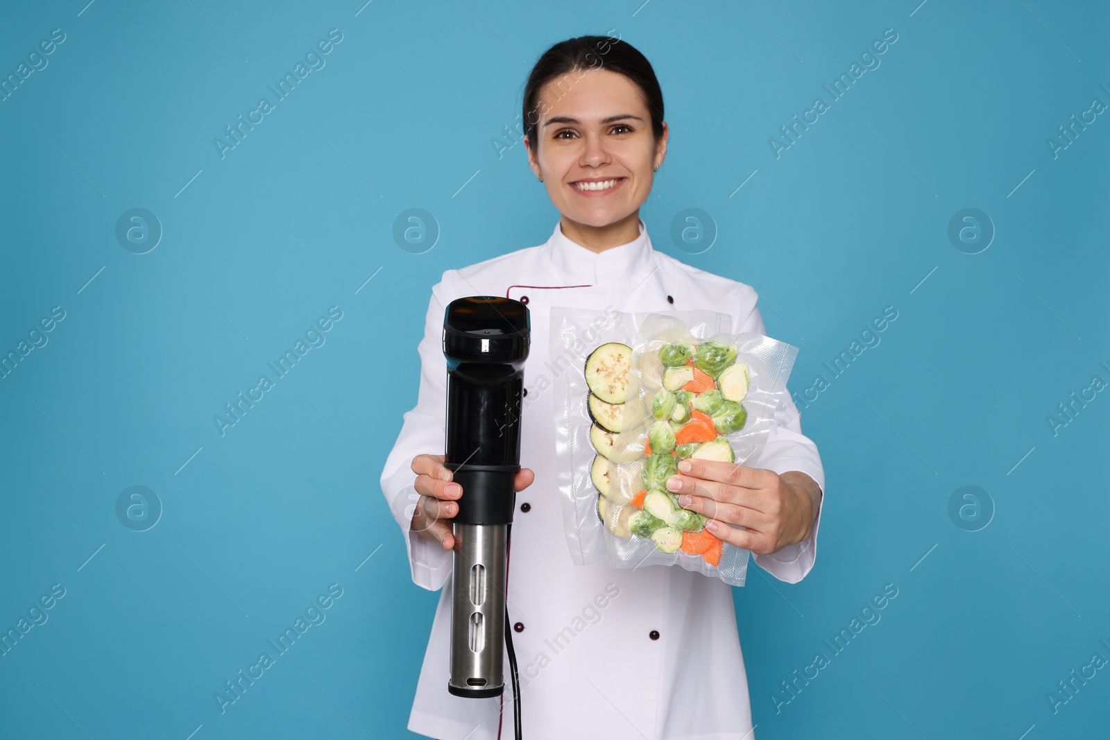 Photo of Chef holding sous vide cooker and vegetables in vacuum packs on light blue background