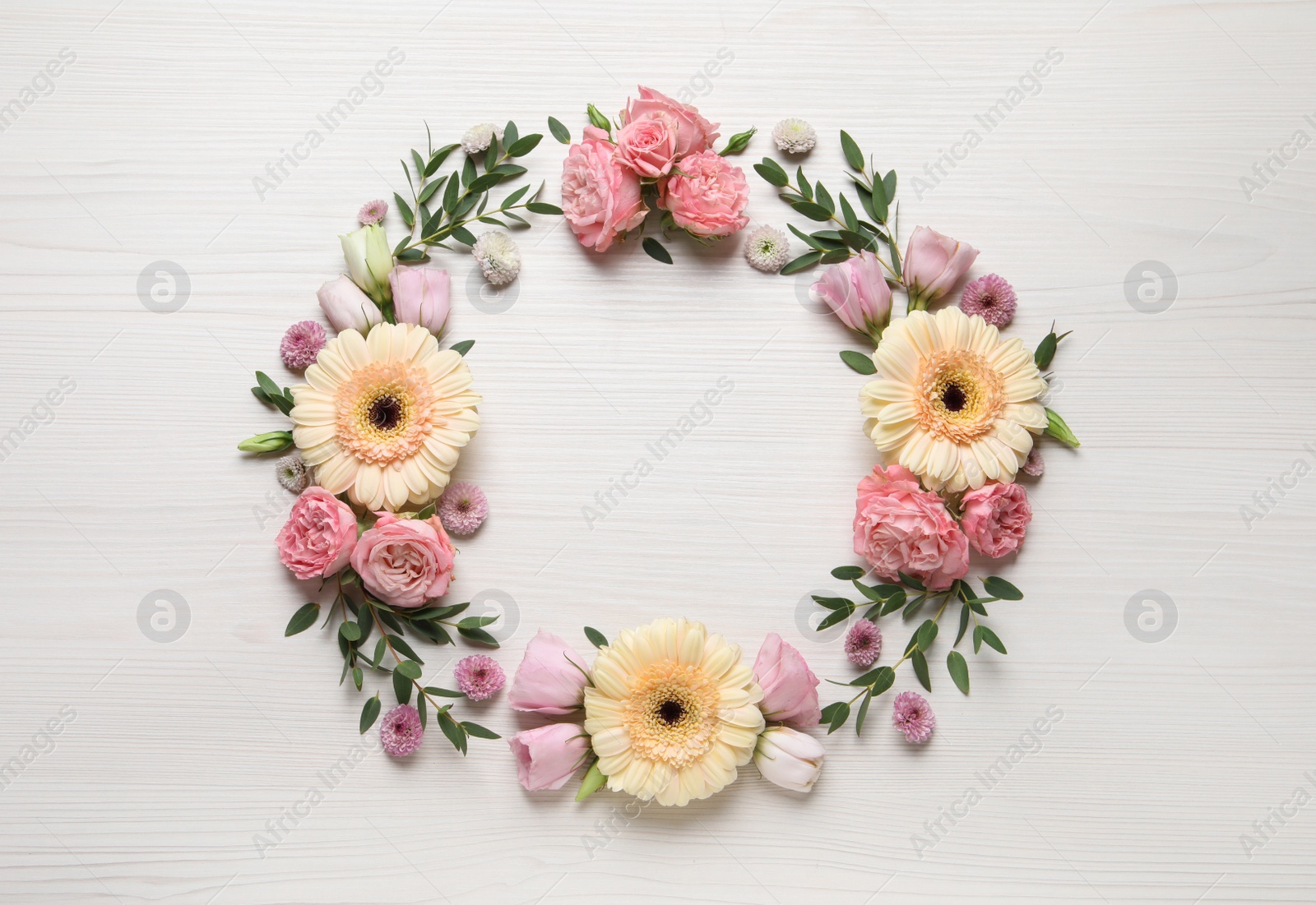 Photo of Wreath made of beautiful flowers and green leaves on white wooden background, flat lay. Space for text